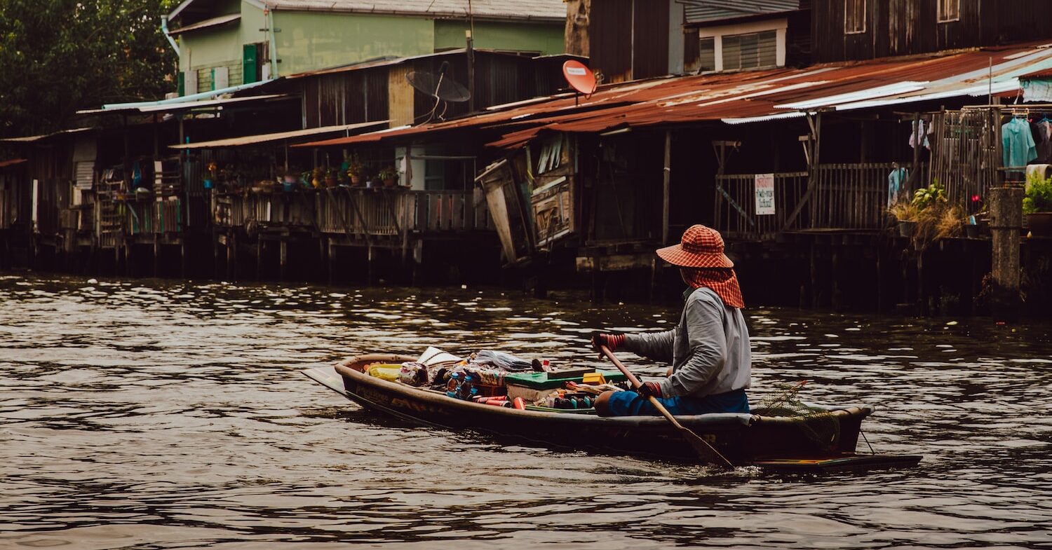 woman riding boat holding paddle on calm body of water in front of houses