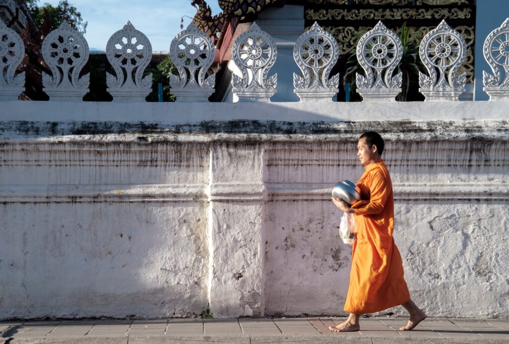 Monk in orange robe, common in Thai Buddhism, walking beside wall